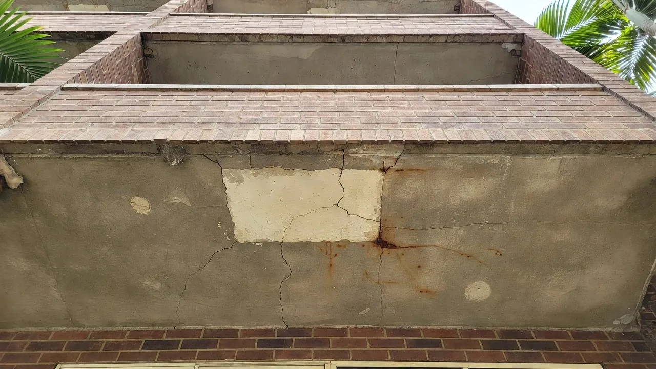 An old painted patch repair on the underside of a balcony slab, with cracks around its edge and fresh rust staining seeping out just beyond it.