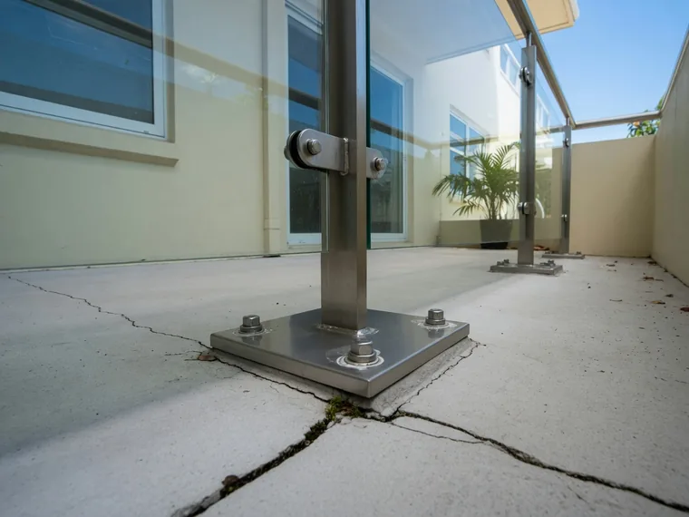 A balustrade base fixing where it meets cracked concrete on an apartment balcony.